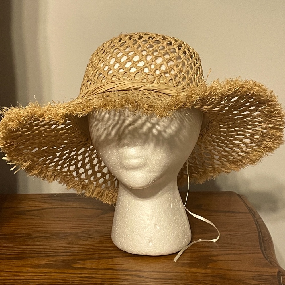 Cute beige hat with straw ribbon. Unique design with holes and fringe around bib